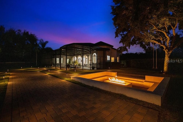 pool at dusk featuring a fire pit and a lanai