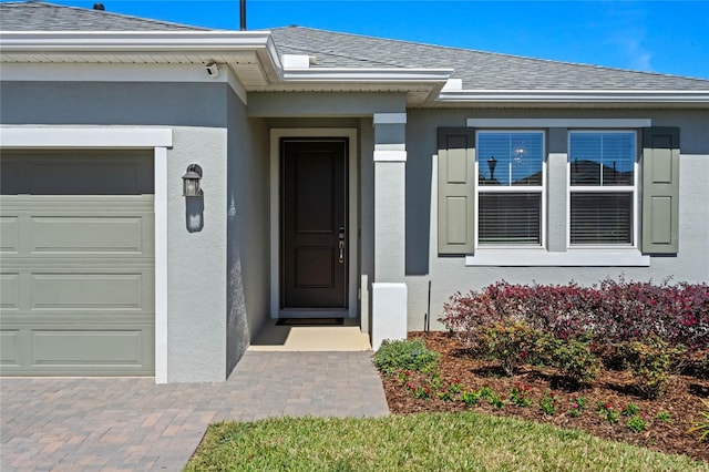 property entrance with stucco siding, roof with shingles, and an attached garage