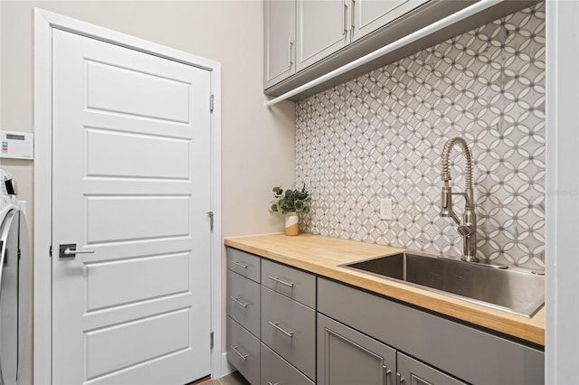 kitchen featuring tasteful backsplash, butcher block countertops, gray cabinets, and a sink