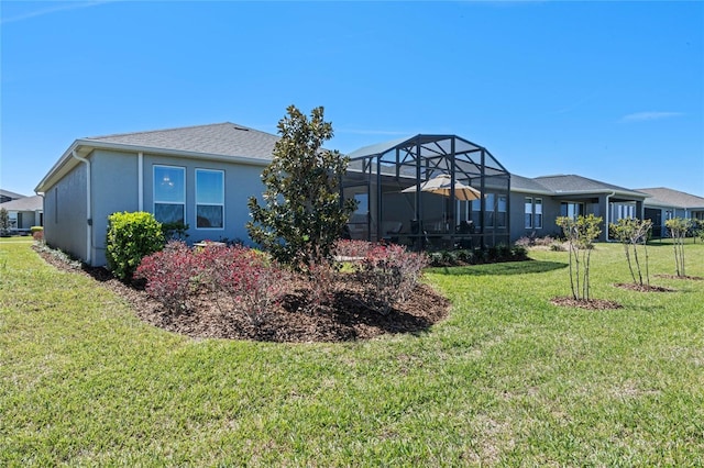 back of house with glass enclosure, a yard, and stucco siding