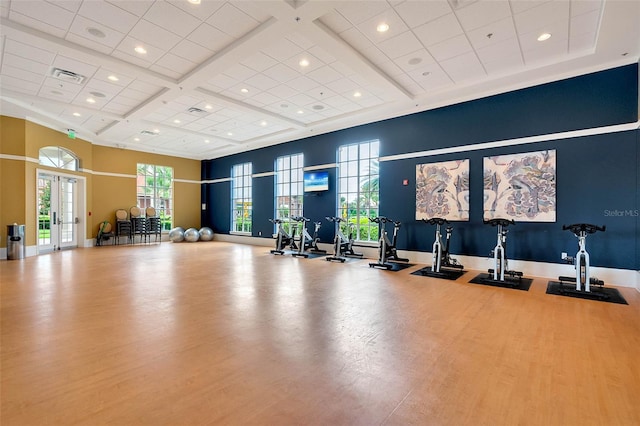 exercise room featuring wood finished floors, baseboards, coffered ceiling, a high ceiling, and french doors