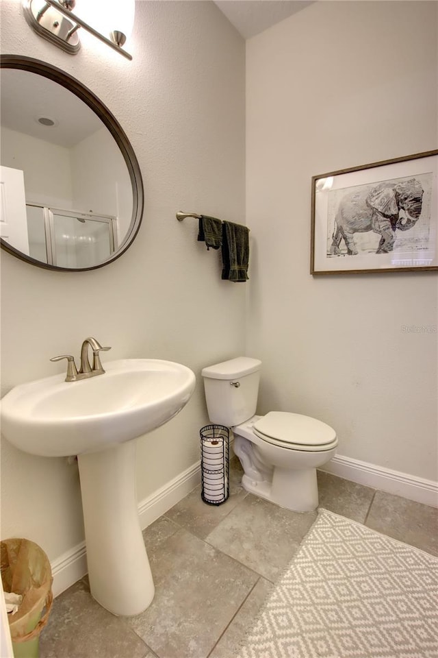 bathroom featuring a shower with shower door, toilet, and baseboards