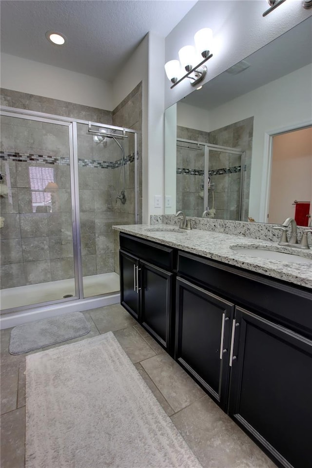 full bath with a sink, a shower stall, a textured ceiling, and double vanity