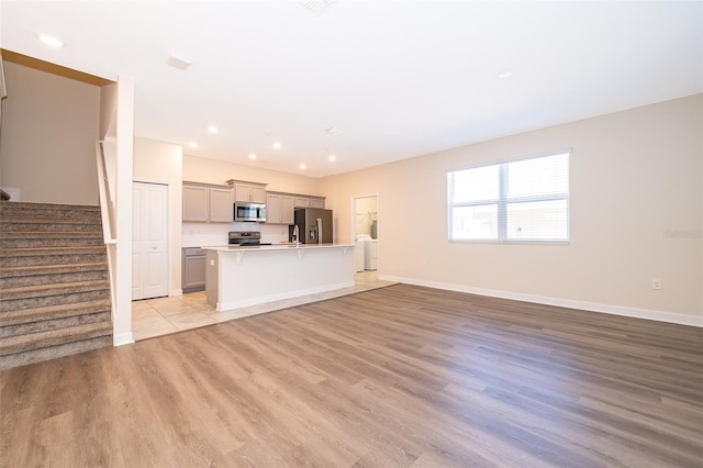 unfurnished living room featuring light wood finished floors, stairs, baseboards, and recessed lighting