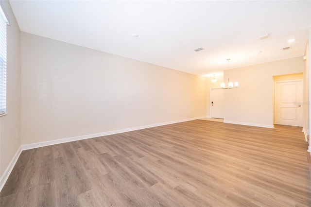 empty room with light wood-type flooring, baseboards, and a chandelier