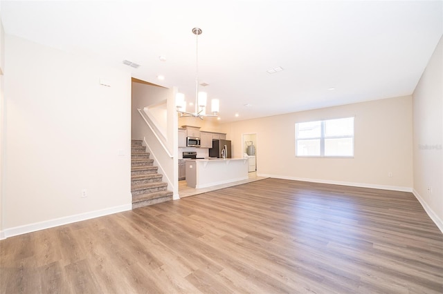 unfurnished living room with visible vents, baseboards, light wood-style flooring, stairway, and a chandelier