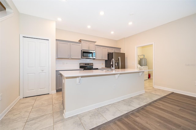 kitchen with a large island, a breakfast bar area, gray cabinets, light countertops, and appliances with stainless steel finishes