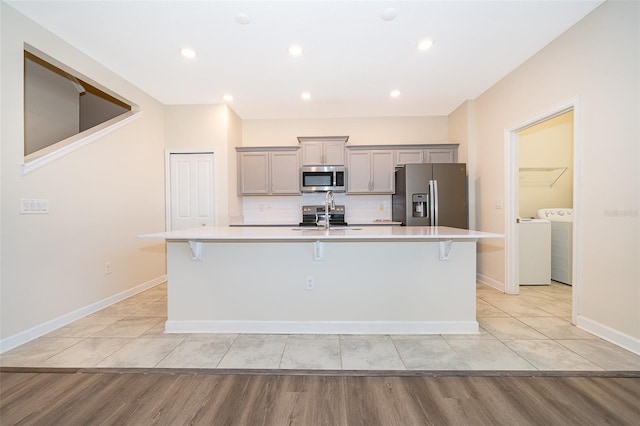 kitchen with a kitchen island with sink, gray cabinetry, stainless steel appliances, a sink, and independent washer and dryer