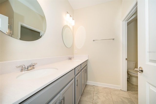 bathroom with baseboards, a sink, toilet, and double vanity