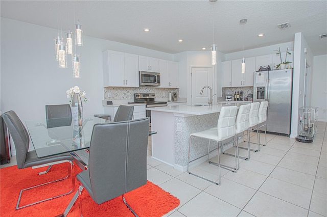 kitchen featuring a sink, light countertops, appliances with stainless steel finishes, white cabinetry, and a kitchen bar