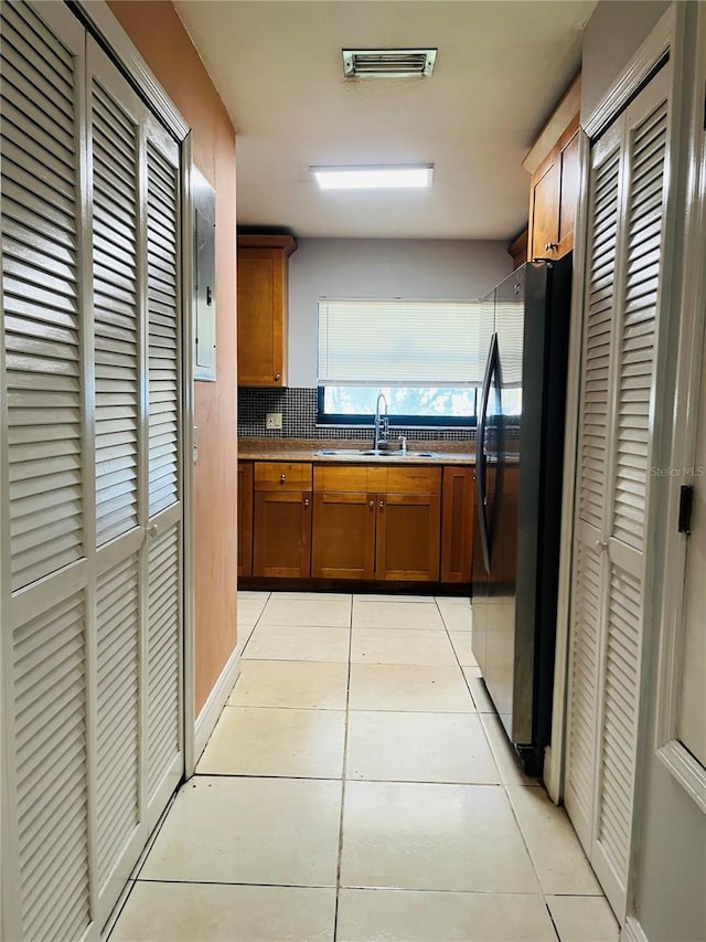 kitchen featuring a sink, light tile patterned flooring, brown cabinetry, and freestanding refrigerator