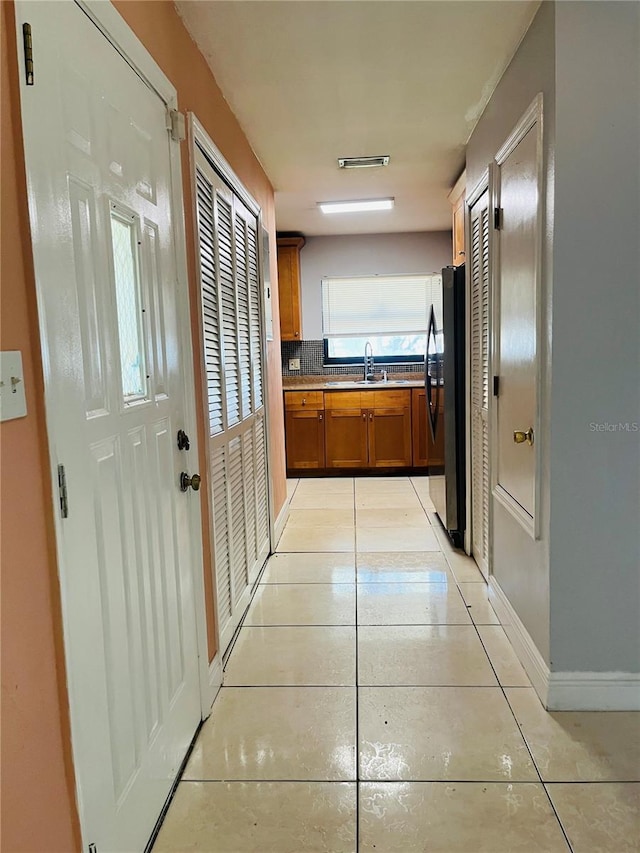 hallway featuring light tile patterned floors, baseboards, and a sink