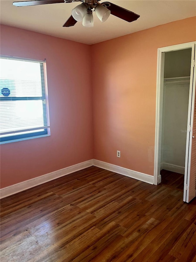 unfurnished bedroom with a closet, baseboards, dark wood-style floors, and a ceiling fan