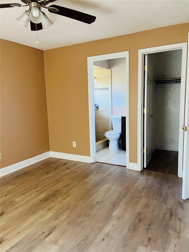 unfurnished bedroom featuring ensuite bath, wood finished floors, a closet, baseboards, and a spacious closet