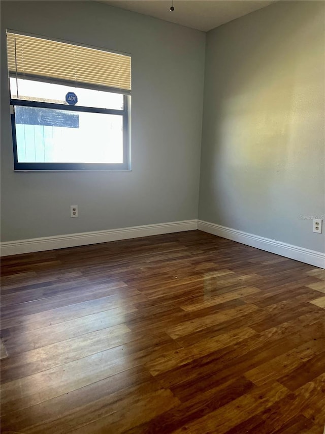 spare room featuring baseboards and dark wood-type flooring