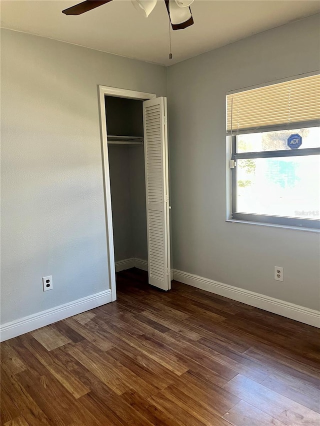 unfurnished bedroom with dark wood-style floors, baseboards, a closet, and ceiling fan