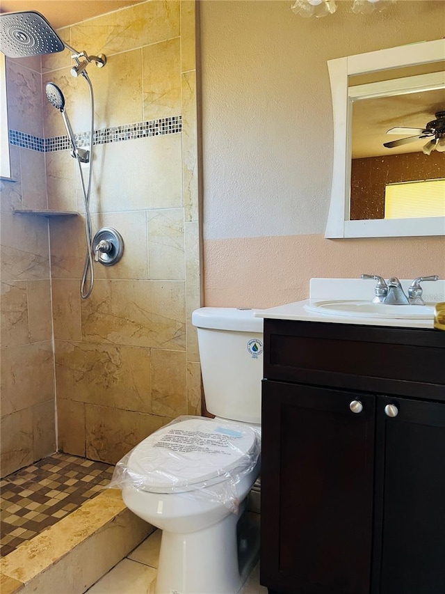 bathroom featuring tiled shower, toilet, vanity, and ceiling fan