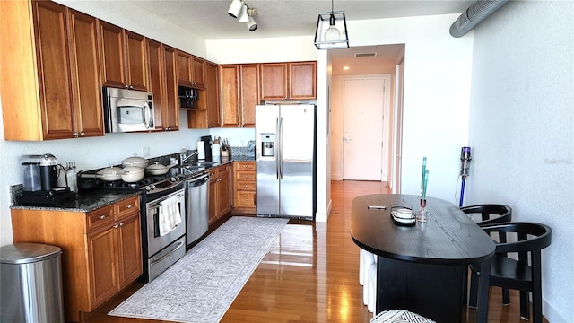 kitchen with brown cabinetry, wood finished floors, visible vents, and appliances with stainless steel finishes