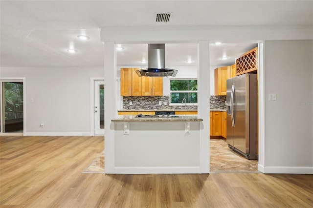 kitchen with light wood finished floors, stainless steel fridge, island range hood, and backsplash