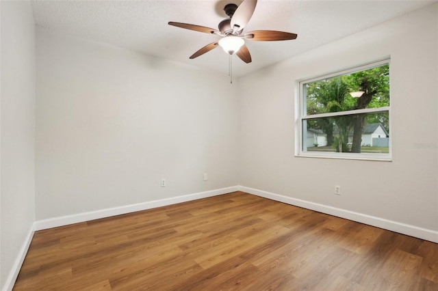 empty room with a textured ceiling, wood finished floors, a ceiling fan, and baseboards