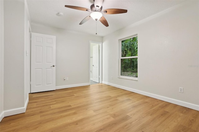 empty room with a textured ceiling, light wood-type flooring, and baseboards