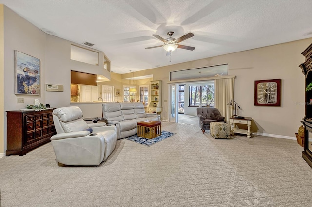 carpeted living area with a textured ceiling, visible vents, baseboards, and ceiling fan