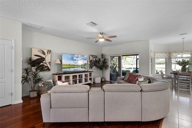 living area featuring visible vents, ceiling fan with notable chandelier, a textured ceiling, and wood finished floors