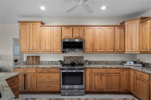 kitchen with light stone counters, recessed lighting, ceiling fan, stainless steel appliances, and a textured ceiling