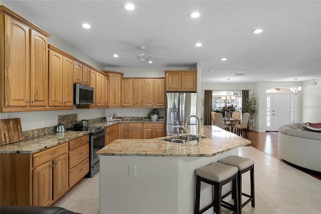 kitchen featuring a kitchen island with sink, a sink, light stone counters, stainless steel appliances, and a breakfast bar area