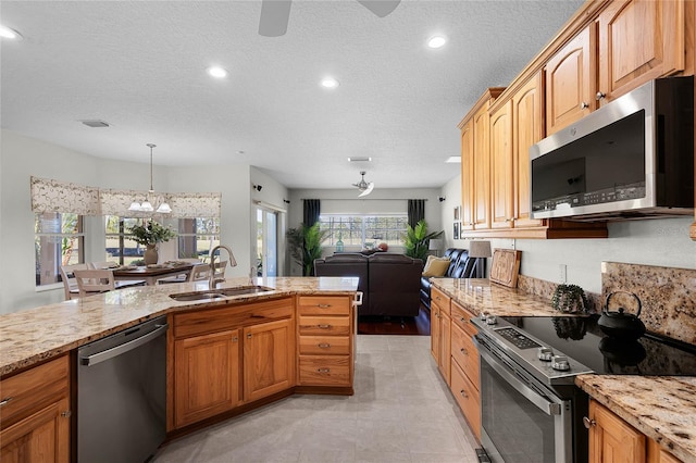 kitchen with light stone counters, a sink, appliances with stainless steel finishes, a textured ceiling, and open floor plan