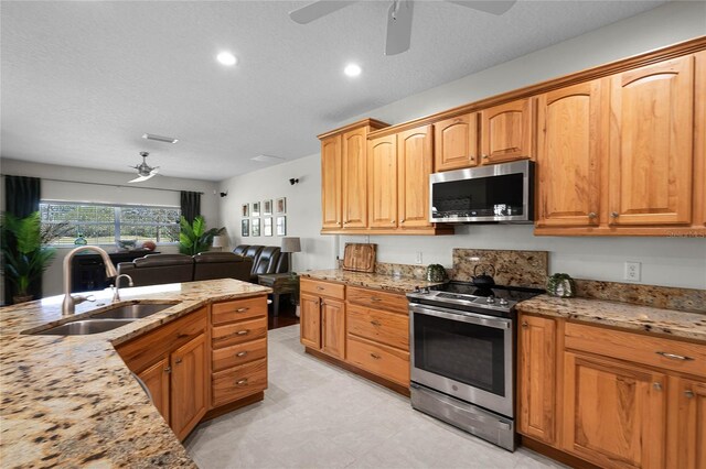 kitchen with a sink, light stone counters, appliances with stainless steel finishes, and open floor plan