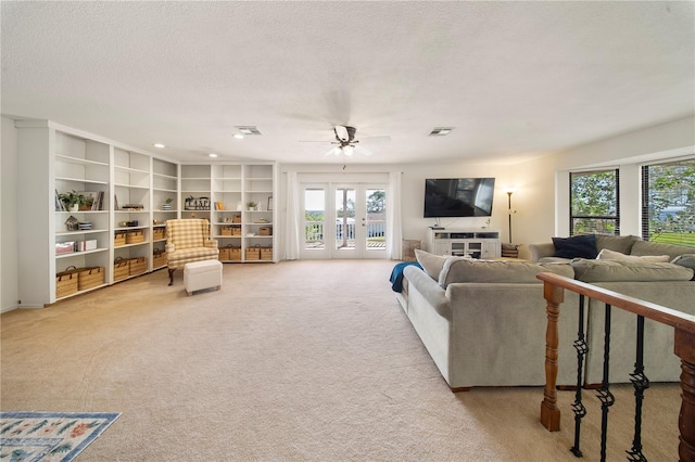 living area with french doors, a textured ceiling, visible vents, and light colored carpet