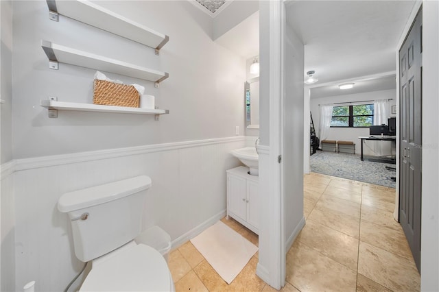 half bathroom featuring tile patterned flooring, a wainscoted wall, and toilet