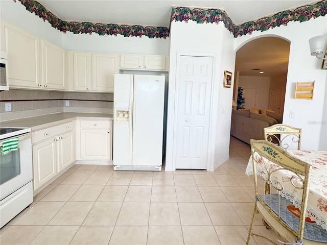 kitchen with light countertops, light tile patterned floors, decorative backsplash, arched walkways, and white appliances