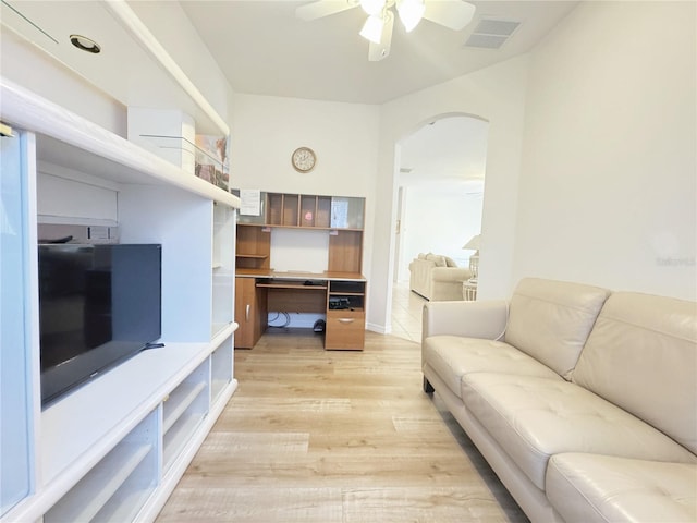 living area with visible vents, arched walkways, light wood finished floors, ceiling fan, and built in study area