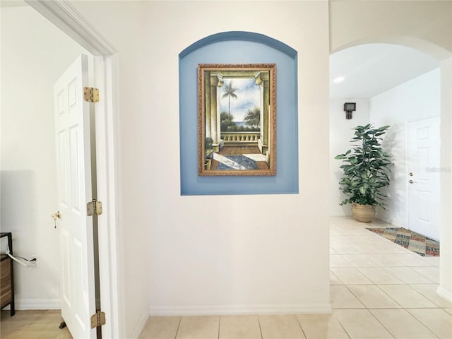 corridor with tile patterned flooring, baseboards, and arched walkways