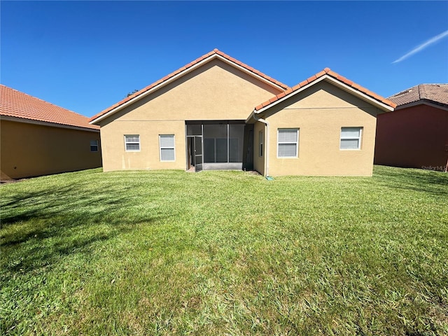 rear view of house featuring stucco siding, a tile roof, a yard, and a sunroom