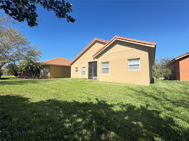 rear view of house with a tile roof, a yard, and stucco siding