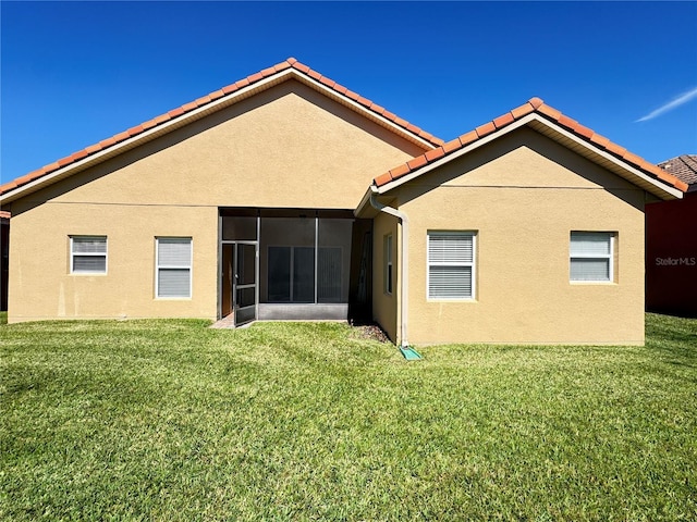 rear view of house with a lawn, a tiled roof, a sunroom, and stucco siding