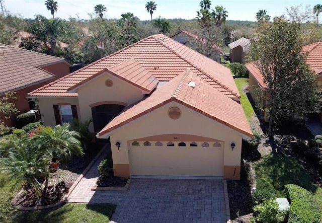 mediterranean / spanish-style home with decorative driveway, a tile roof, an attached garage, and stucco siding