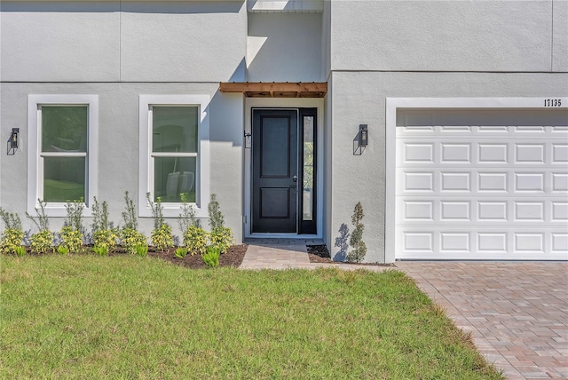 property entrance featuring decorative driveway, a lawn, and stucco siding