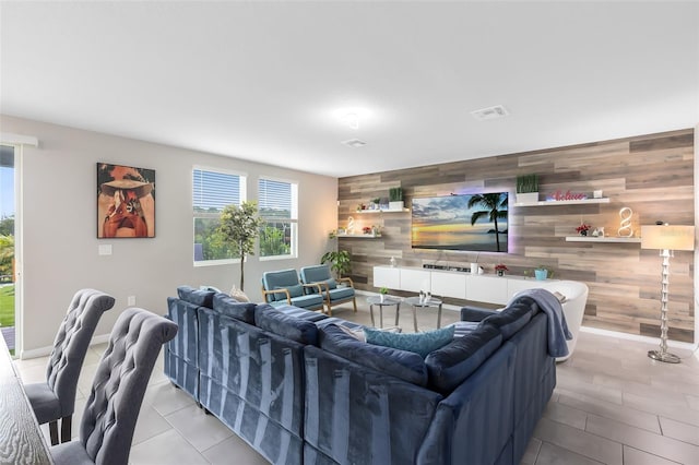 tiled living room with an accent wall, baseboards, visible vents, and wood walls