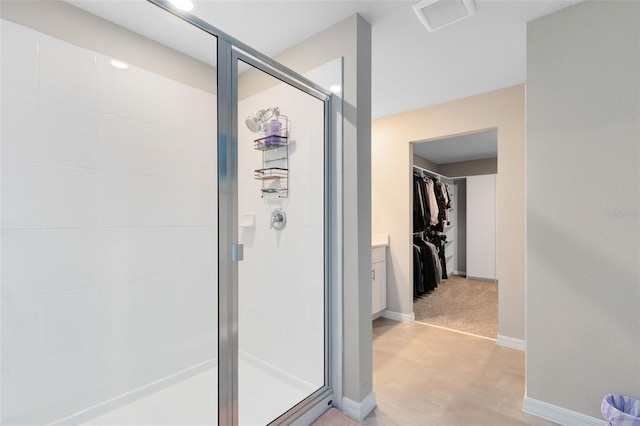 bathroom with visible vents, a shower stall, a walk in closet, and baseboards