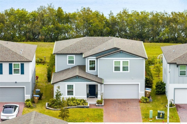 view of front of property with decorative driveway, a front yard, an attached garage, and a shingled roof