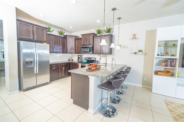 kitchen featuring light stone counters, a peninsula, light tile patterned flooring, stainless steel appliances, and dark brown cabinetry