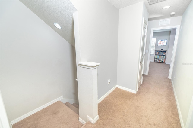 hall with an upstairs landing, light carpet, a textured ceiling, and baseboards