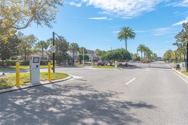view of asphalt road with curbs, a gate, a gated entry, and street lights