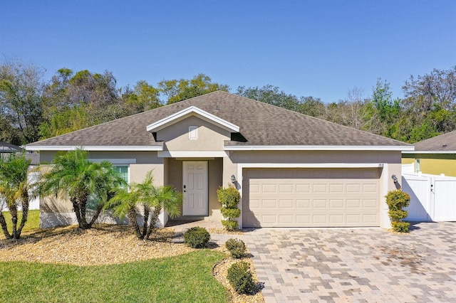 single story home featuring a gate, fence, an attached garage, stucco siding, and decorative driveway