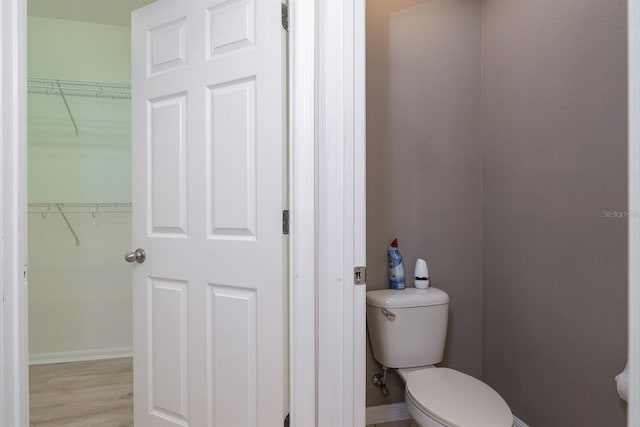 bathroom featuring a spacious closet, toilet, wood finished floors, and baseboards