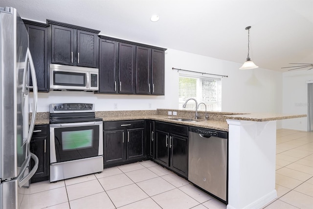 kitchen featuring light tile patterned floors, light stone countertops, a peninsula, a sink, and appliances with stainless steel finishes